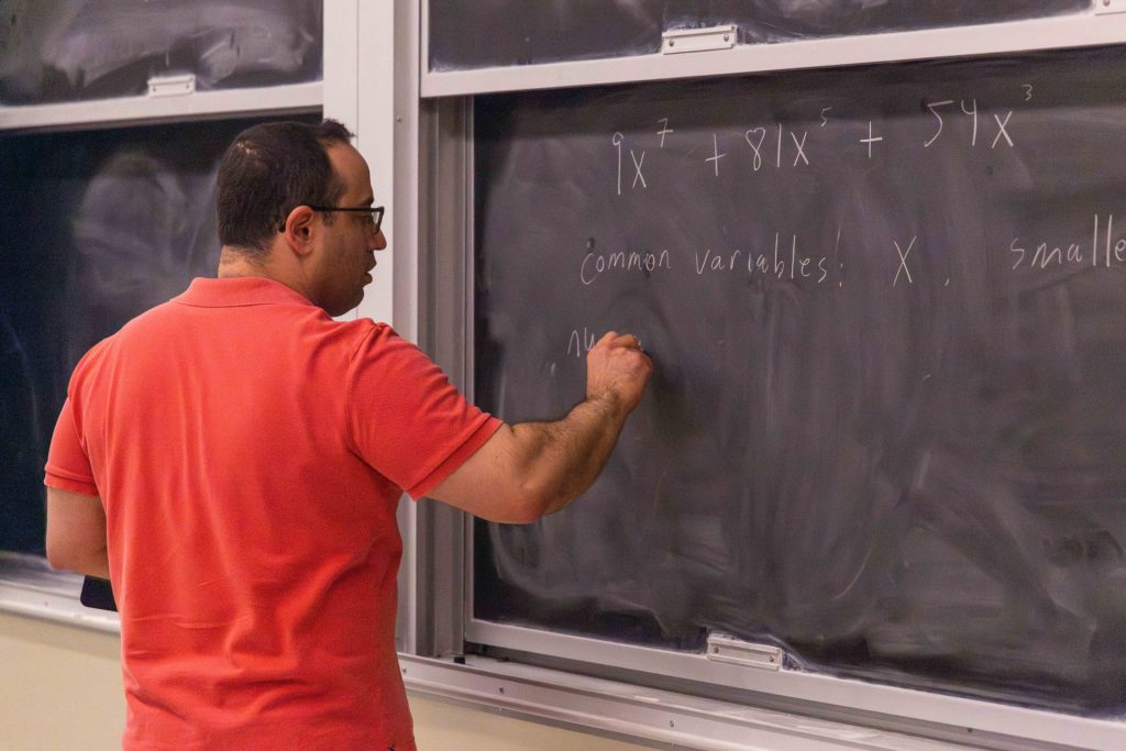 A SUNY Oneonta professor writes on a blackboard with chalk.