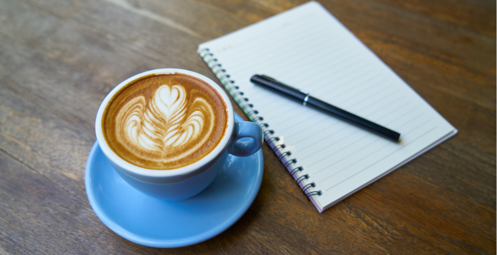 A latte in a blue mug and an open notebook