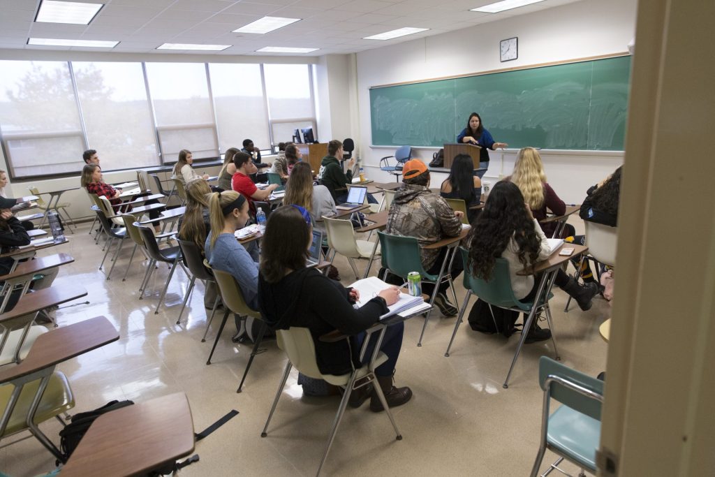 A SUNY Oneonta faculty member stands in front of a chalkboard while speaking to a room of students